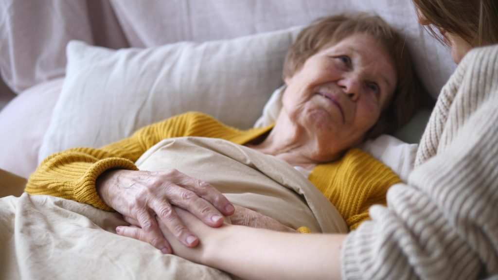 Personne tenant la main d'une femme âgée allongée dans son lit
