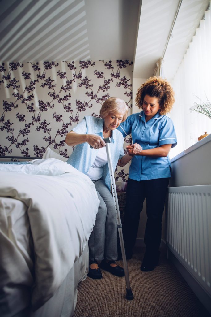 aide-soignante aidant une femme âgée avec une canne à se lever de son lit