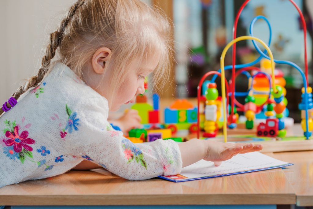 petite fille blonde s'amusant avec des jeux assise à une table