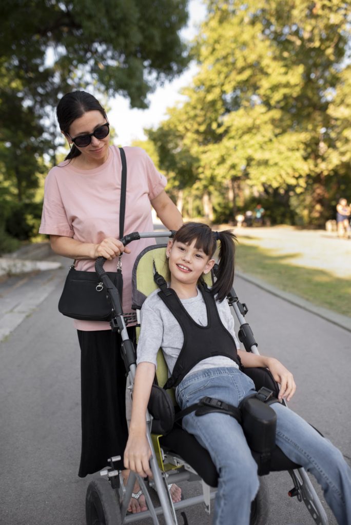 femme poussant une petite fille brune en fauteuil roulant