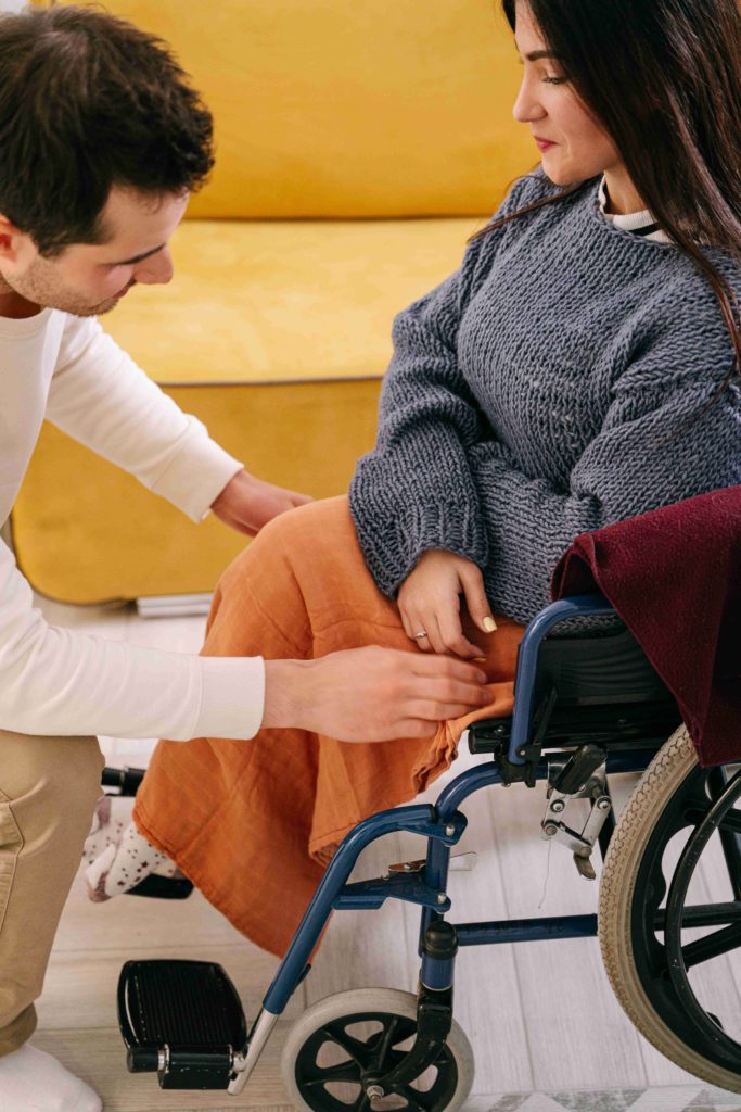 auxiliaire de vie mettant une couverture sur les jambe d'une femme assise sur un fauteuil roulant