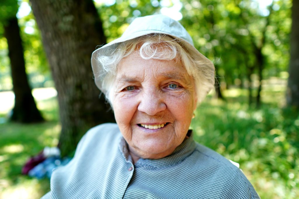 femme agée qui sourit portant un chapeau dans u nparc